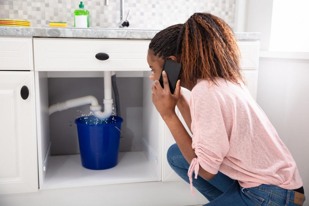 Femme appelant plombier devant de fuite tuyau d’évier