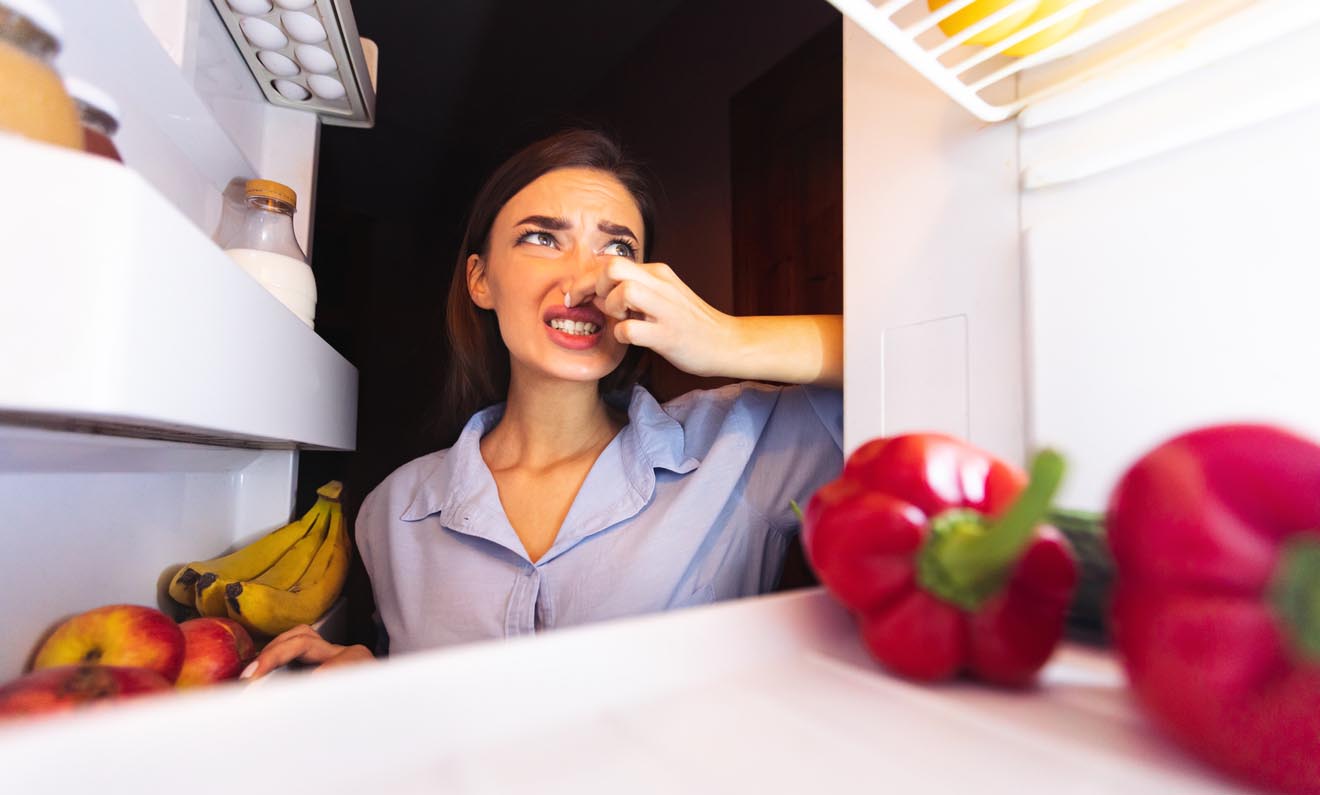Femme se bouche le nez en ouvrant son frigo