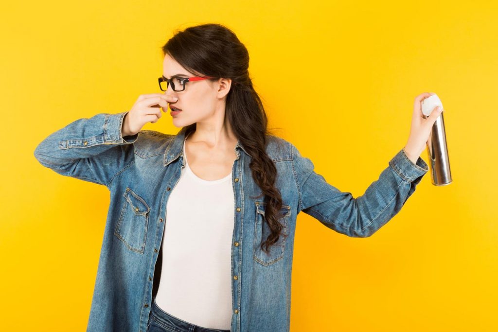 femme se bouche le nez et met du spray