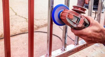 Main D'une Personne Tenant Une Ponceuse électrique Qui Ponce Une Barrière En Fer