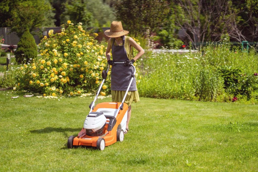 Une jeune fille en chapeau de paille tond une pelouse