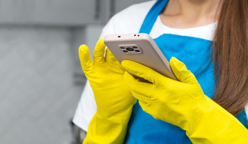 femme portant des gants de caoutchouc jaunes et un tablier bleu tenant un smartphone