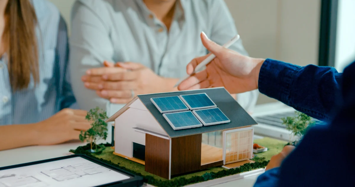 Un couple et un assureur discutent autour d’une maison miniature éco-responsable
