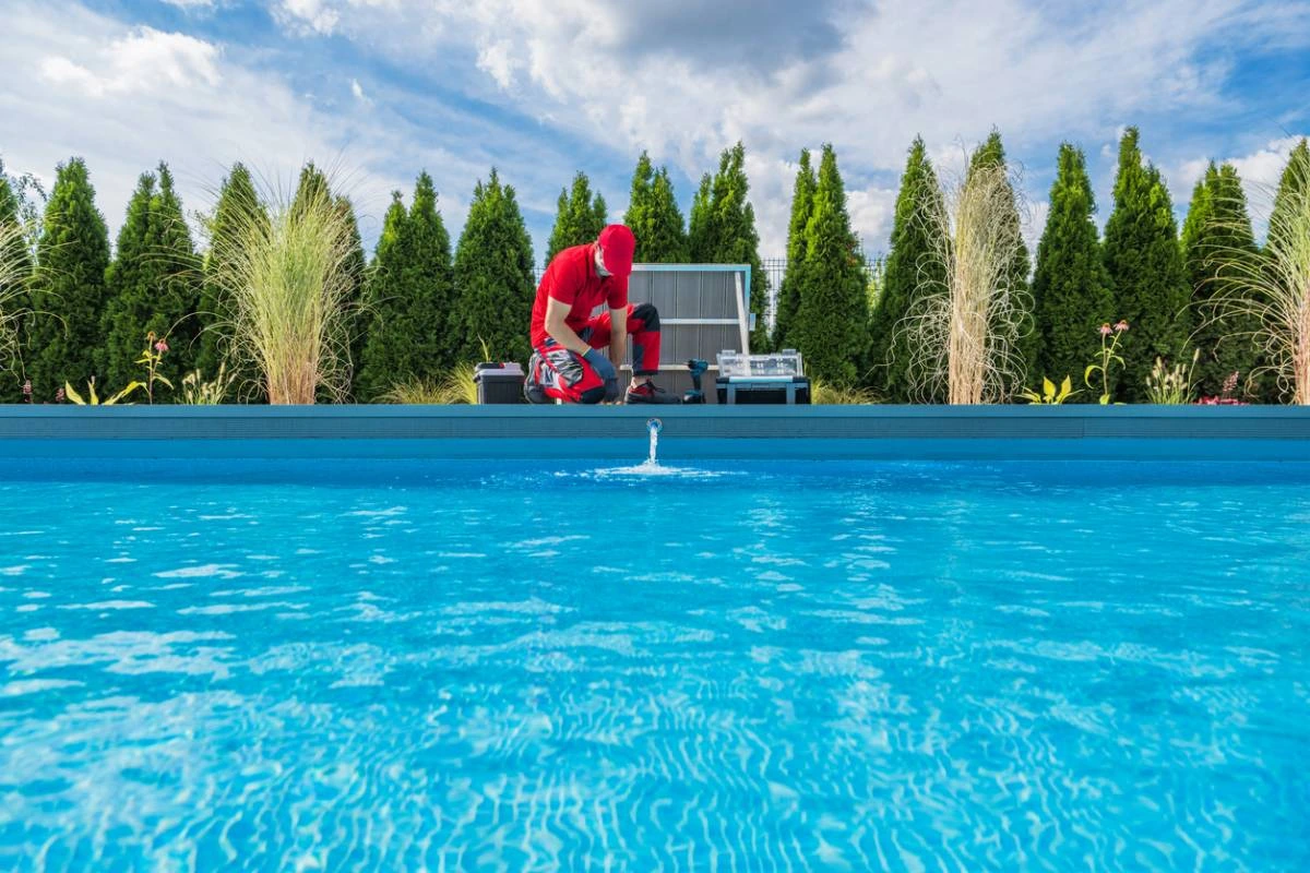 Technicien effectuant un entretien piscine dans un jardin paysagé, face à une eau limpide et bien traitée.
