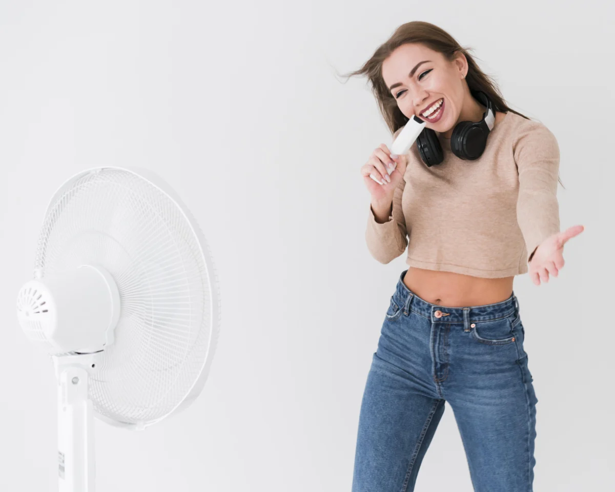 Dans un appartement lumineux, une femme chante devant un ventilateur mobile blanc