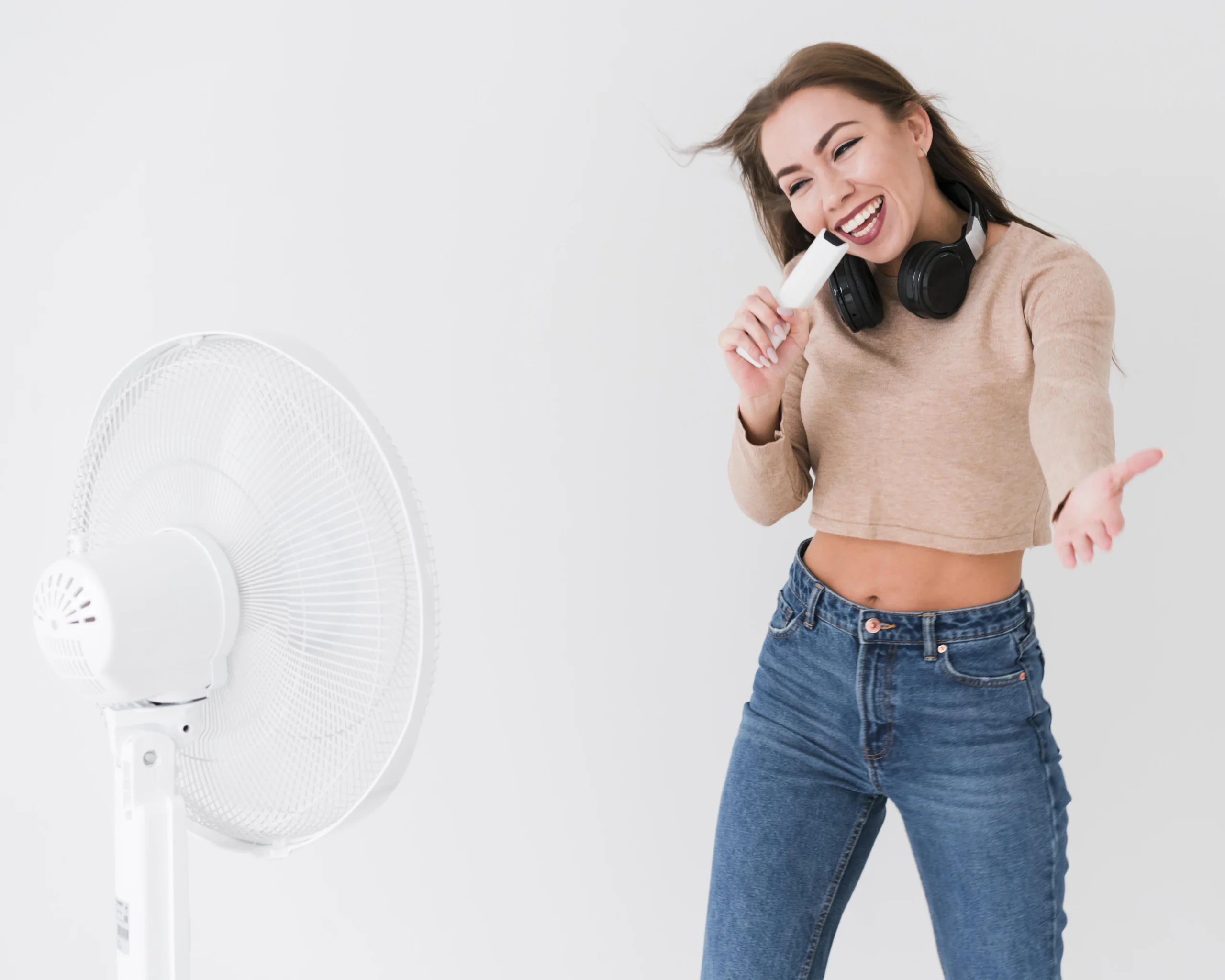 Dans un appartement lumineux, une femme chante devant un ventilateur mobile blanc